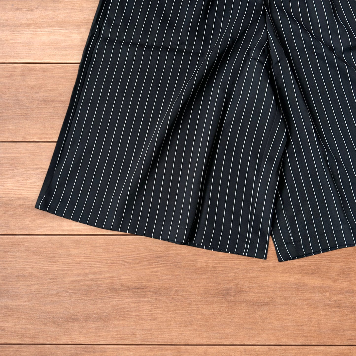 Black vintage style baggy wide long tailored shorts with white pinstripes laid flat on wooden surface