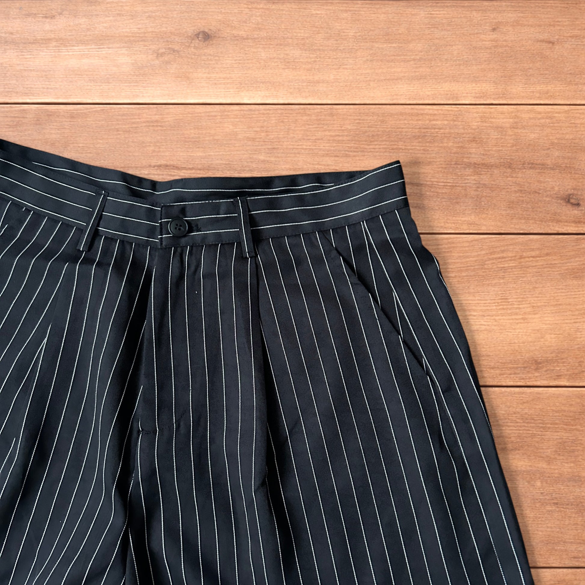 Black vintage style baggy wide long tailored shorts with white pinstripes laid flat on wooden surface