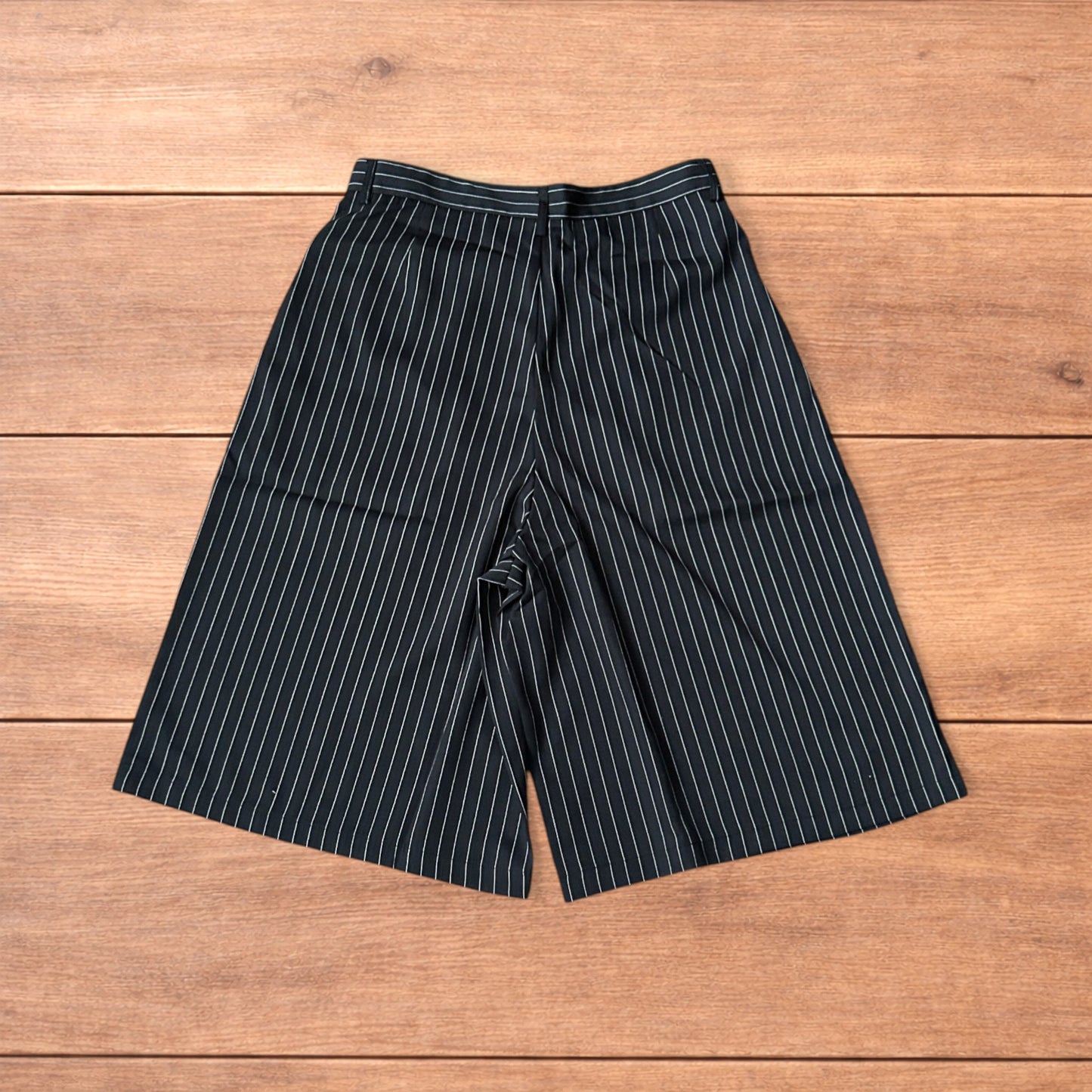 Black vintage style baggy wide long tailored shorts with white pinstripes laid flat on wooden surface