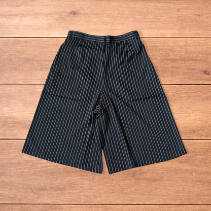 Black vintage style baggy wide long tailored shorts with white pinstripes laid flat on wooden surface