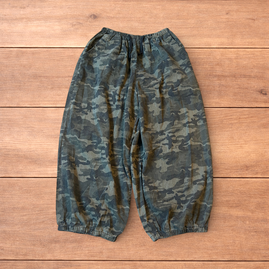 Super baggy wide leg parachute joggers trousers in army camo with elasticated waistband and drawstrings laid flat on wooden floor