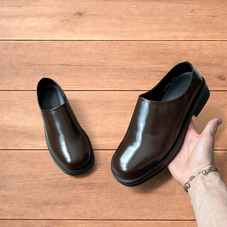 Pair of brown faux leather slip-on loafers shoes with black soles held against a wooden floor background