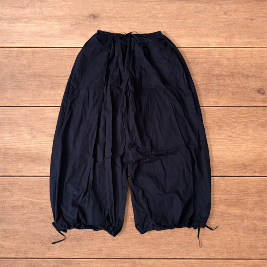 Super baggy wide leg black flight pants with drawstring waist and ankle ties laid flat on wood floor.