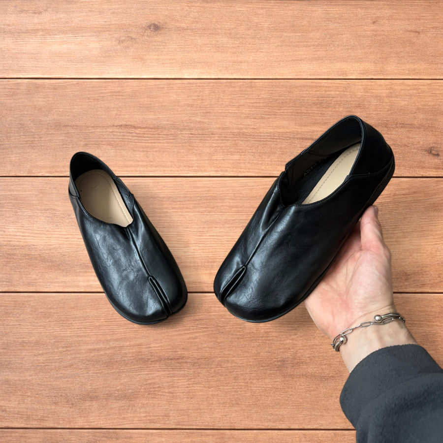 Vintage style black faux leather tabi split toe shoes on wooden surface held in hand