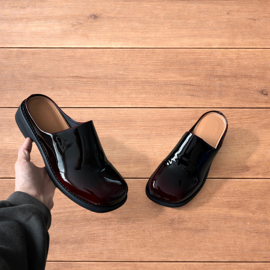 Glossy oxblood red faux leather slip on clogs slippers with black soles on wooden floor