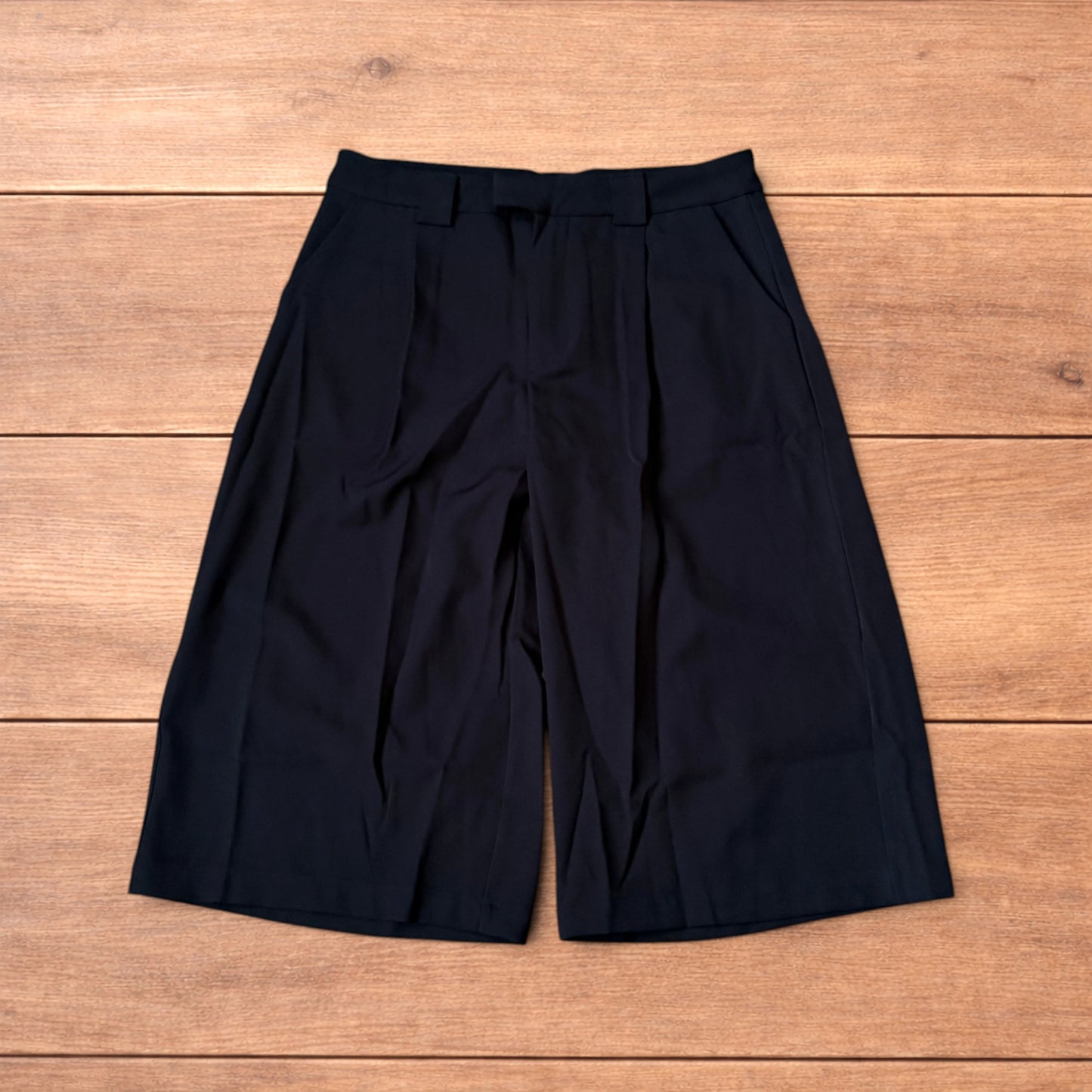 Black vintage style baggy wide leg tailored shorts laid flat on wooden floor showing front and back views