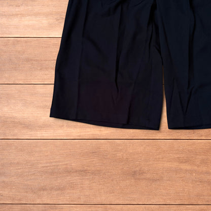 Black vintage style baggy wide leg tailored shorts laid flat on wooden floor showing front and back views