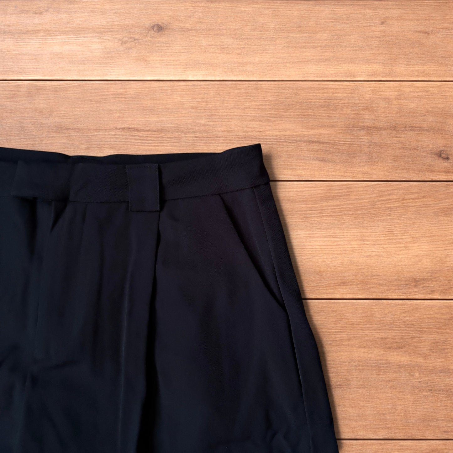 Black vintage style baggy wide leg tailored shorts laid flat on wooden floor showing front and back views