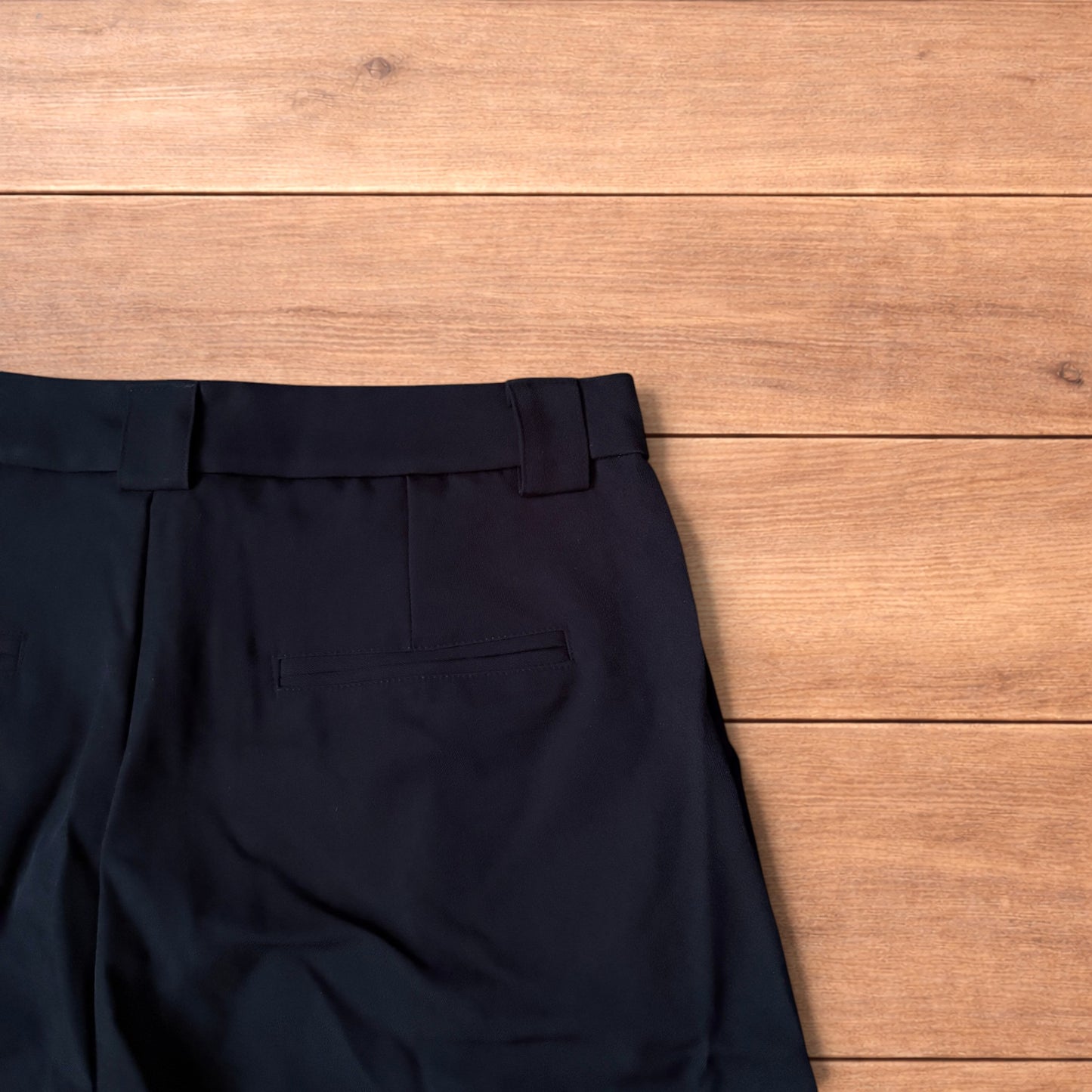 Black vintage style baggy wide leg tailored shorts laid flat on wooden floor showing front and back views