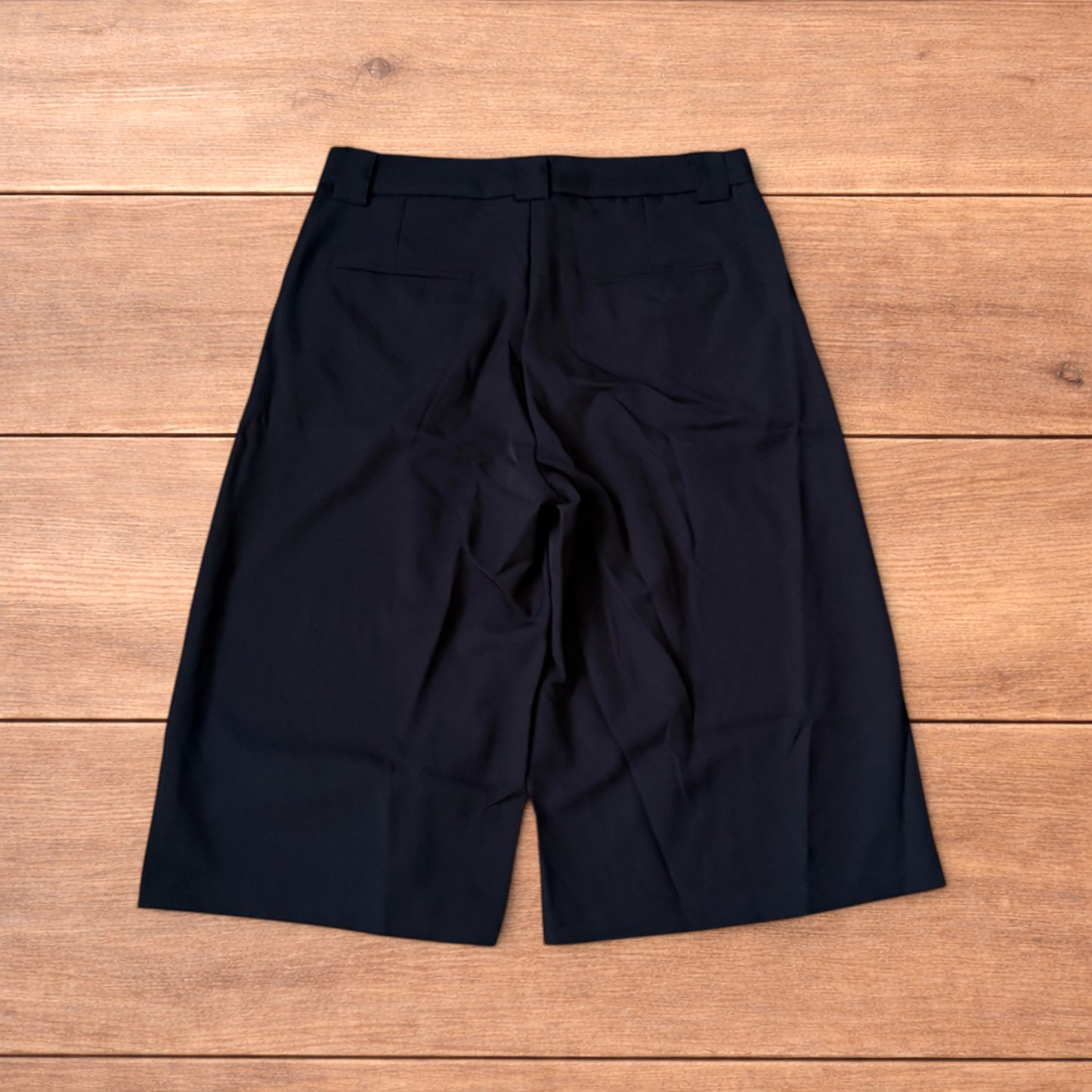 Black vintage style baggy wide leg tailored shorts laid flat on wooden floor showing front and back views