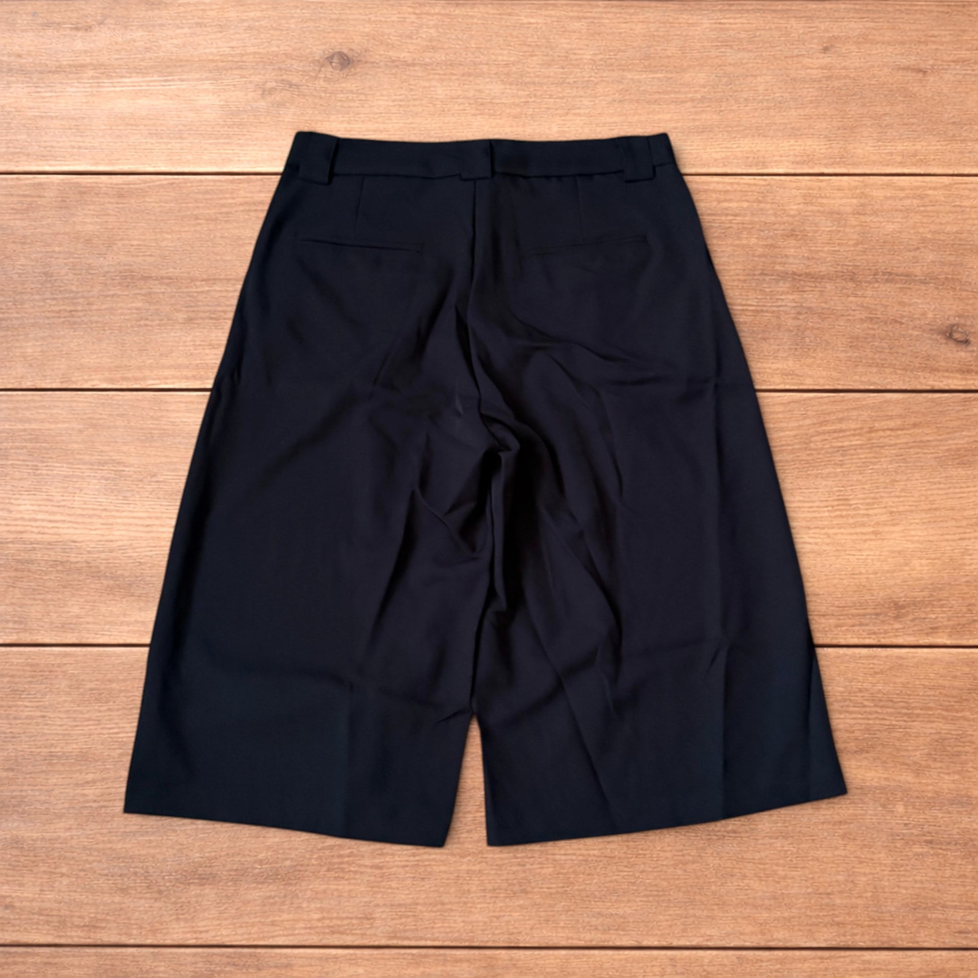 Black vintage style baggy wide leg tailored shorts laid flat on wooden floor showing front and back views