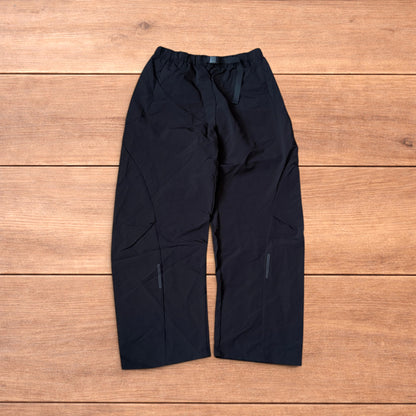 Baggy black gorpcore tech hiking pants with adjustable belted waist laid flat on wooden surface