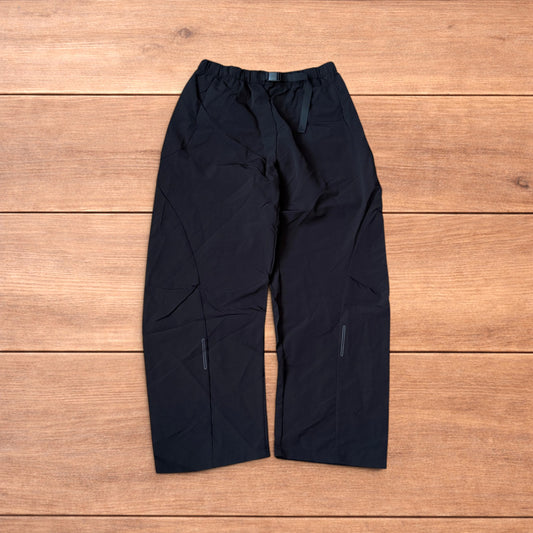 Baggy black gorpcore tech hiking pants with adjustable belted waist laid flat on wooden surface