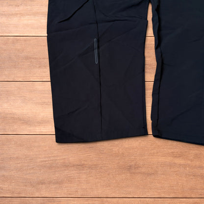 Baggy black gorpcore tech hiking pants with adjustable belted waist laid flat on wooden surface