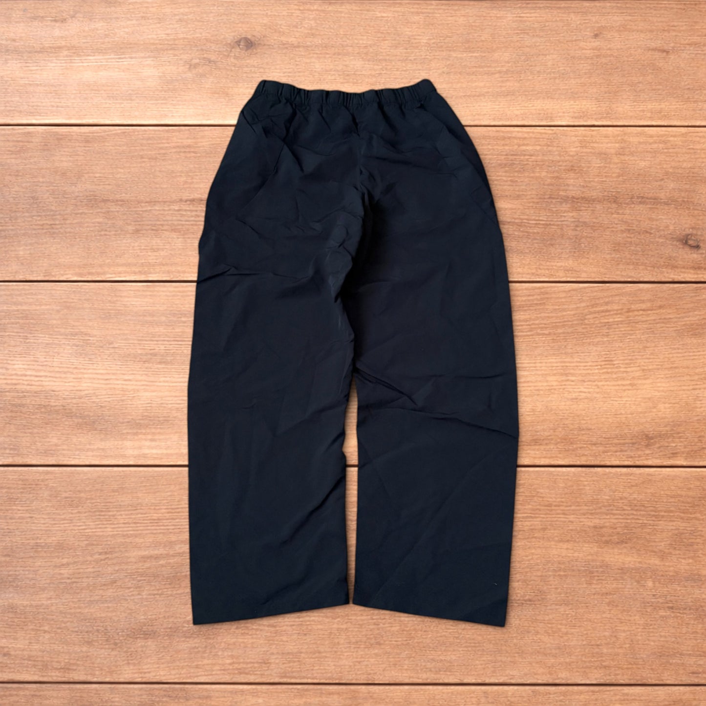 Baggy black gorpcore tech hiking pants with adjustable belted waist laid flat on wooden surface