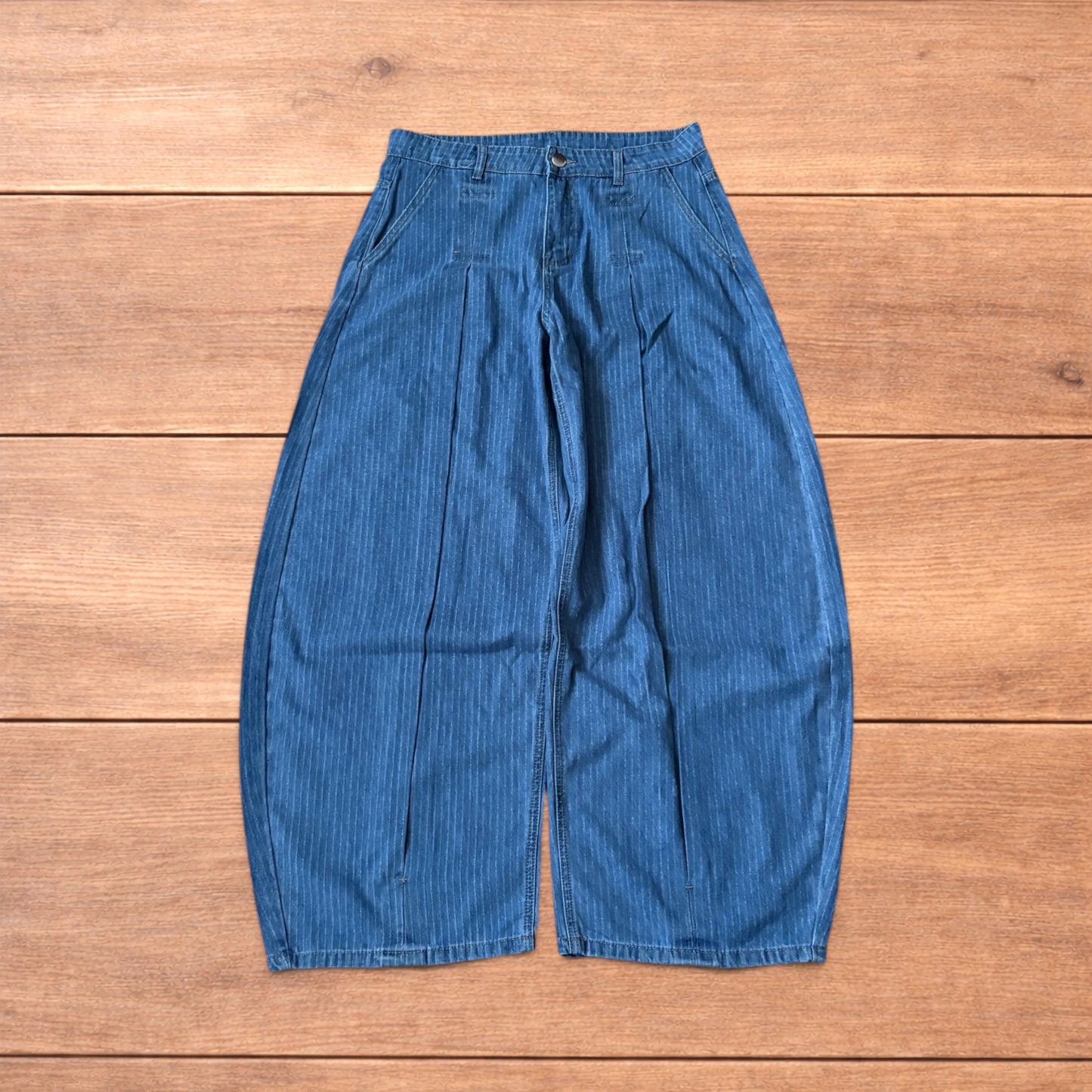 Vintage mid blue pinstripe baggy wide leg jeans with pleats laid flat on wooden surface