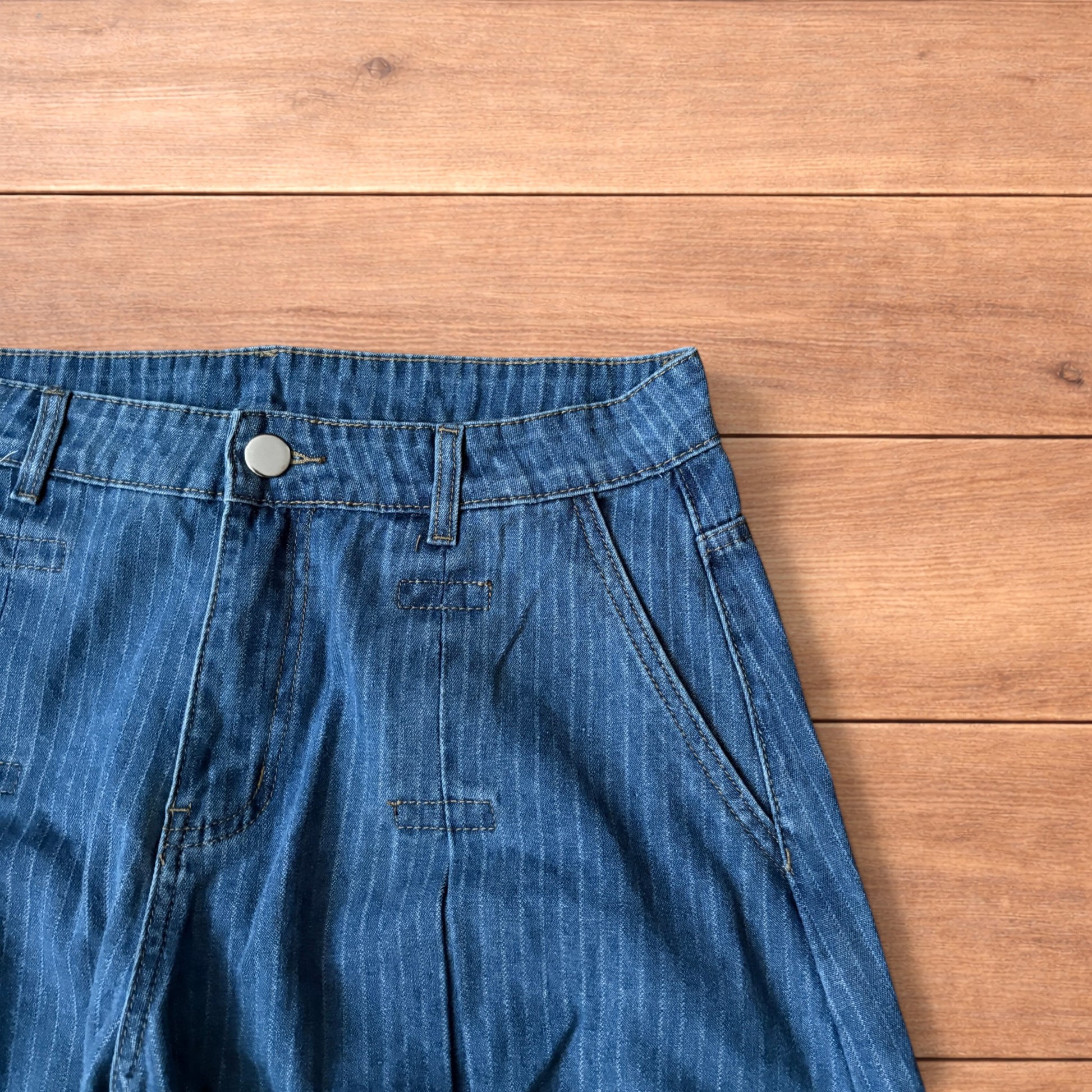 Vintage mid blue pinstripe baggy wide leg jeans with pleats laid flat on wooden surface