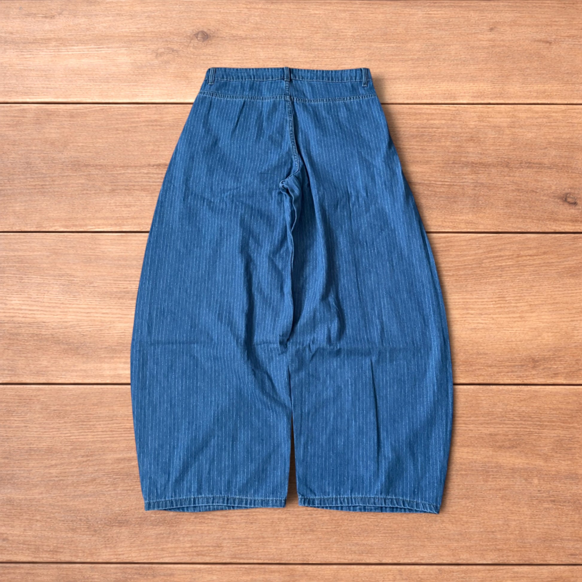 Vintage mid blue pinstripe baggy wide leg jeans with pleats laid flat on wooden surface