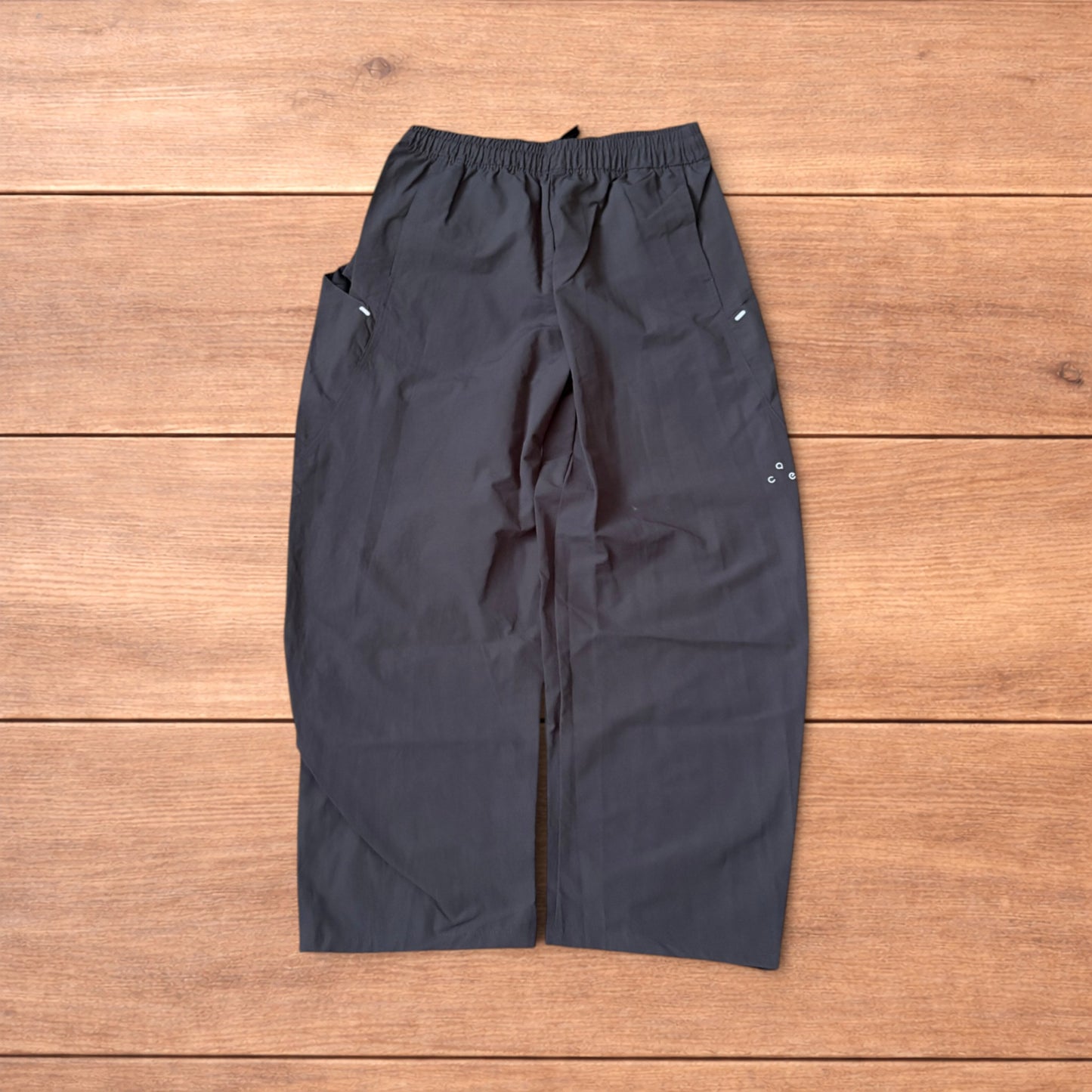 Grey baggy hiking trousers laid flat showing elasticated waistband and side pockets with branding