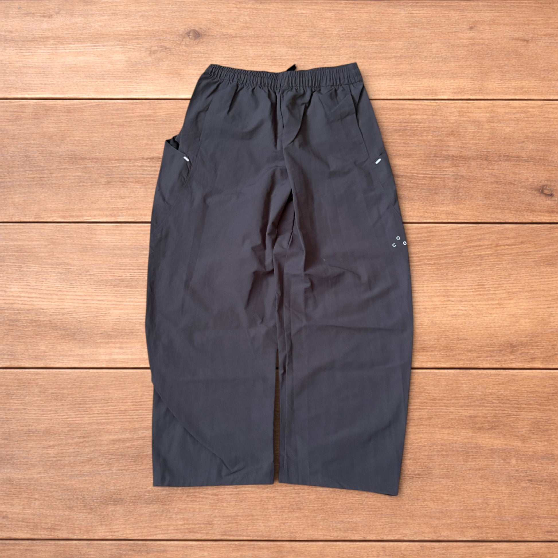 Grey baggy hiking trousers laid flat showing elasticated waistband and side pockets with branding