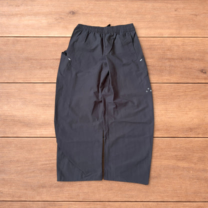 Grey baggy hiking trousers laid flat showing elasticated waistband and side pockets with branding