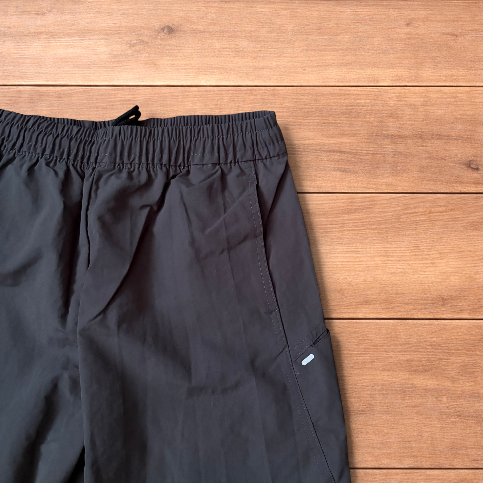 Grey baggy hiking trousers laid flat showing elasticated waistband and side pockets with branding