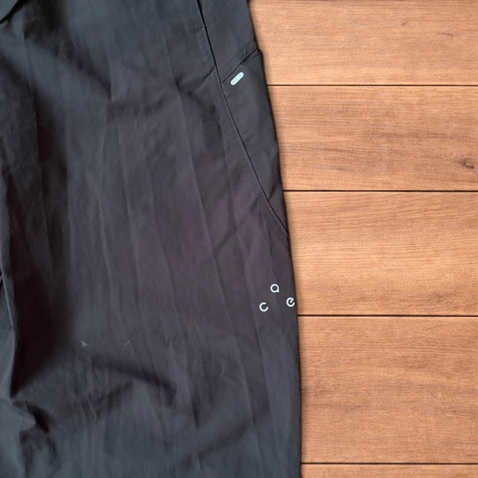 Grey baggy hiking trousers laid flat showing elasticated waistband and side pockets with branding