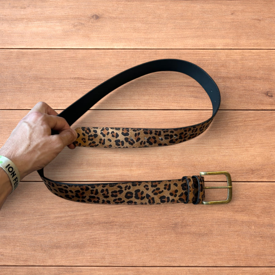 Vintage style faux leather western belt with leopard print and bronze buckle on wooden surface