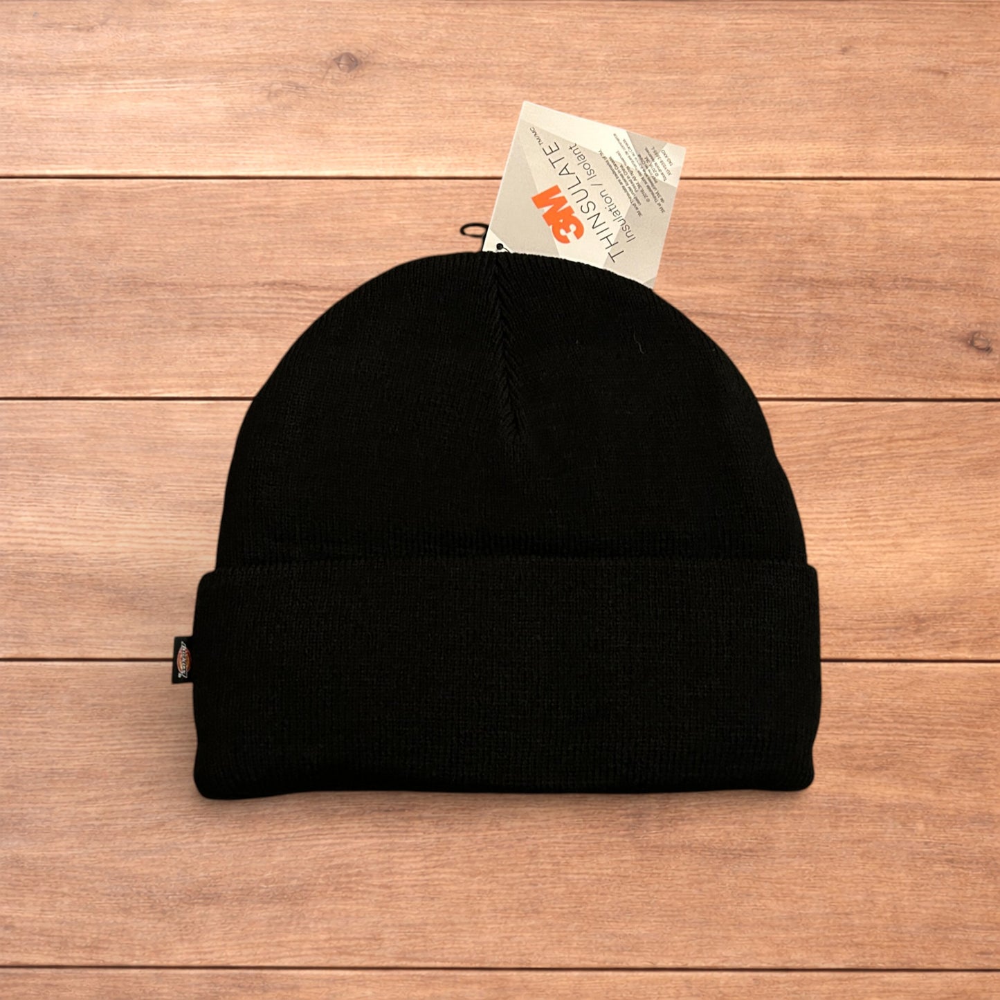 Black Dickies 3M Thinsulate beanie with patch logo on folded cuff, laid flat on wooden surface.