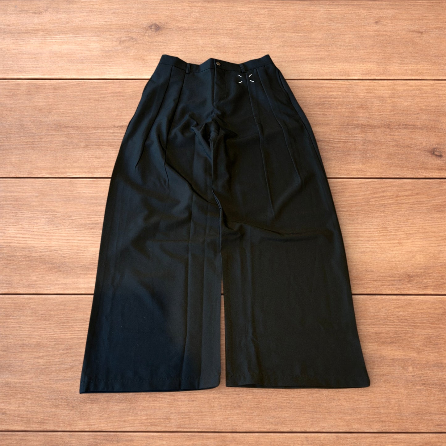 Black vintage style baggy wide leg tailored trousers with pleats and white stitching detail laid flat on wooden surface