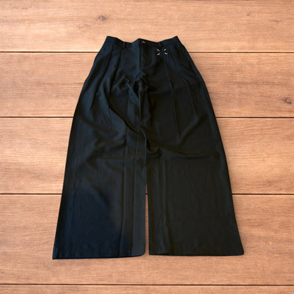 Black vintage style baggy wide leg tailored trousers with pleats and white stitching detail laid flat on wooden surface