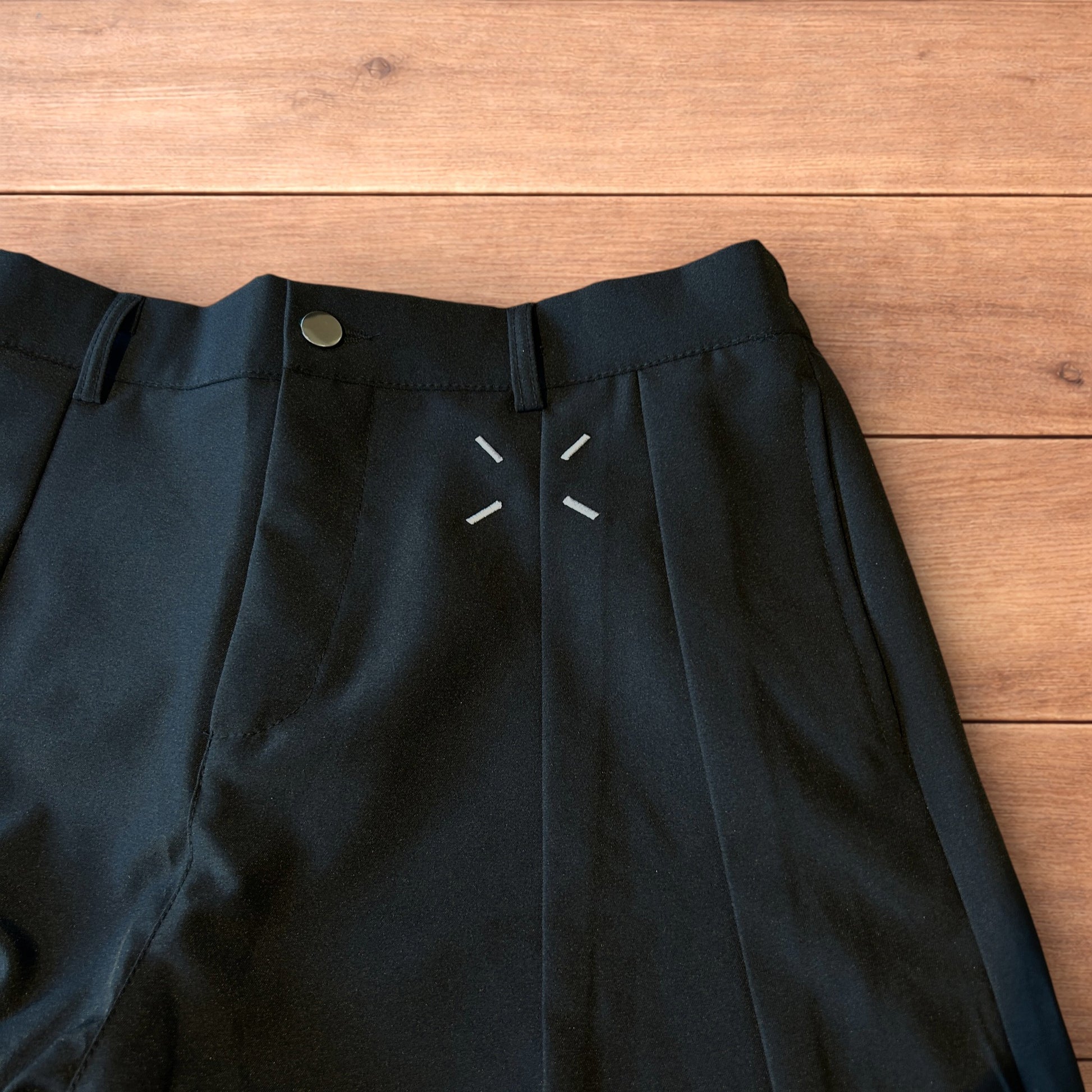 Black vintage style baggy wide leg tailored trousers with pleats and white stitching detail laid flat on wooden surface