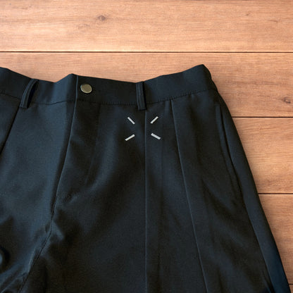 Black vintage style baggy wide leg tailored trousers with pleats and white stitching detail laid flat on wooden surface
