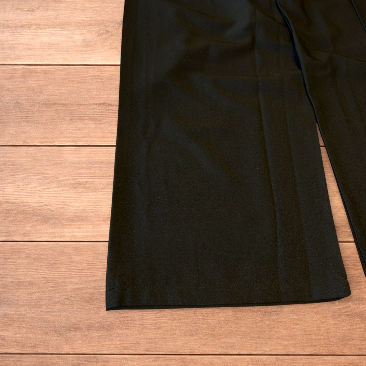 Black vintage style baggy wide leg tailored trousers with pleats and white stitching detail laid flat on wooden surface