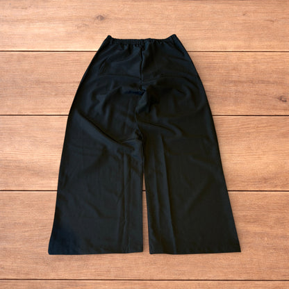 Black vintage style baggy wide leg tailored trousers with pleats and white stitching detail laid flat on wooden surface
