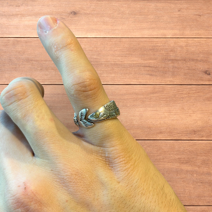 Silver wraparound ring with detailed fish design worn on finger and shown from multiple angles on wooden background.