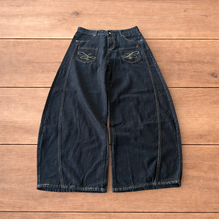 Black vintage style baggy wide leg Korean fit jeans with yellow embroidery on front pockets laid flat on wooden floor