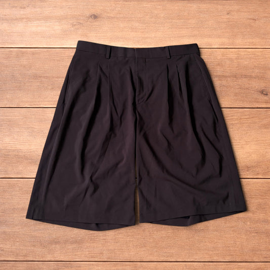 Dark brown vintage style baggy wide leg tailored shorts with front pleats and side pockets laid flat on wooden surface
