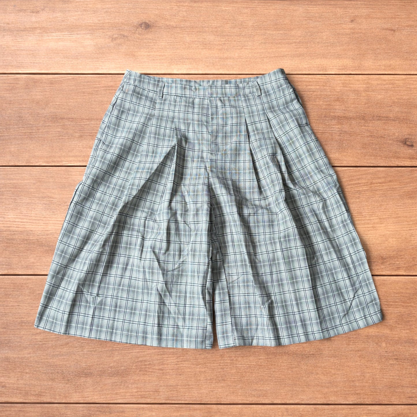 Baggy wide leg shorts with grey, beige and white checkered pattern laid flat on wooden floor showing front and back views