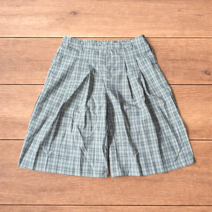 Baggy wide leg shorts with grey, beige and white checkered pattern laid flat on wooden floor showing front and back views