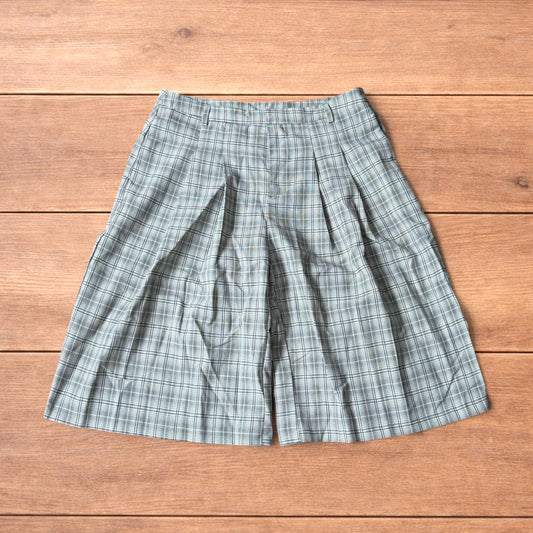 Baggy wide leg shorts with grey, beige and white checkered pattern laid flat on wooden floor showing front and back views
