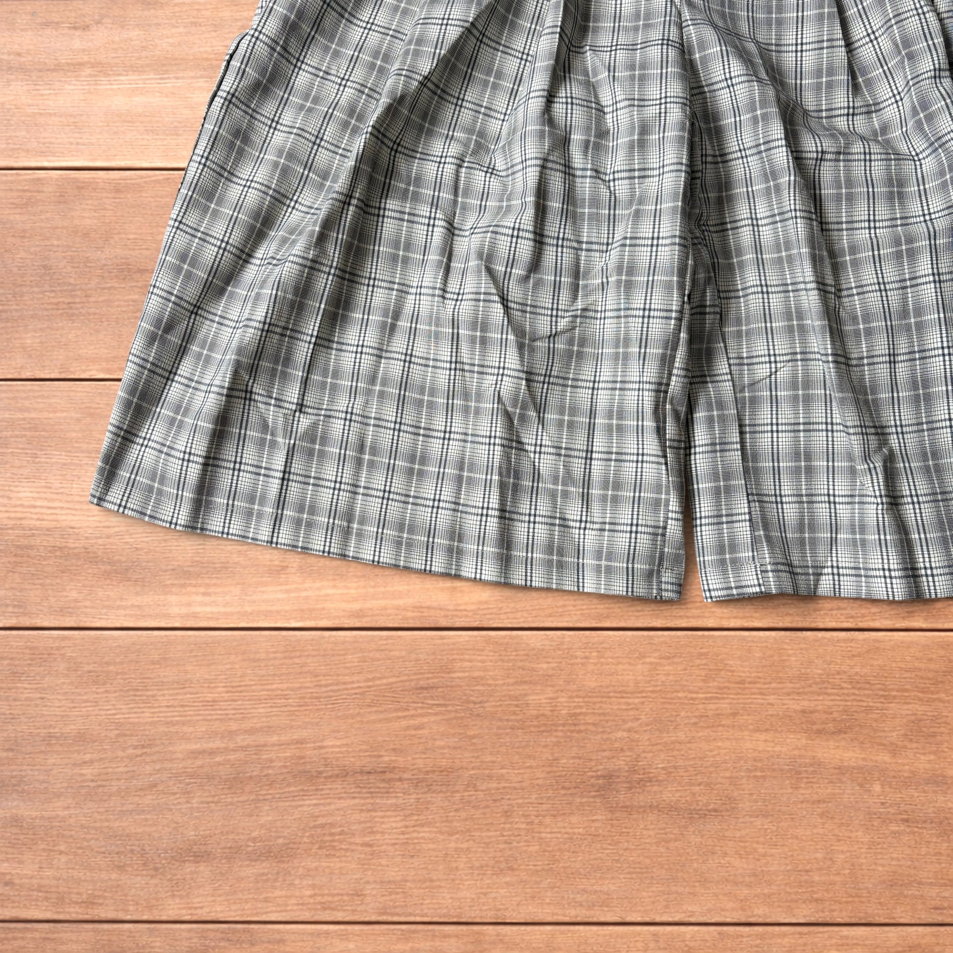 Baggy wide leg shorts with grey, beige and white checkered pattern laid flat on wooden floor showing front and back views
