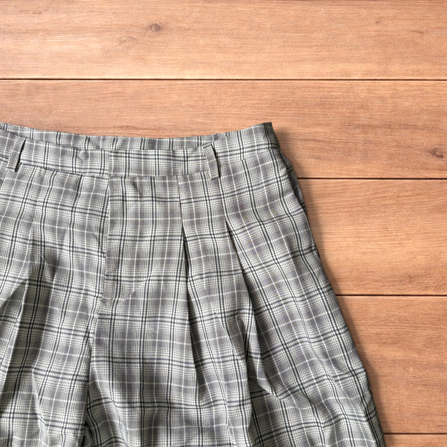 Baggy wide leg shorts with grey, beige and white checkered pattern laid flat on wooden floor showing front and back views