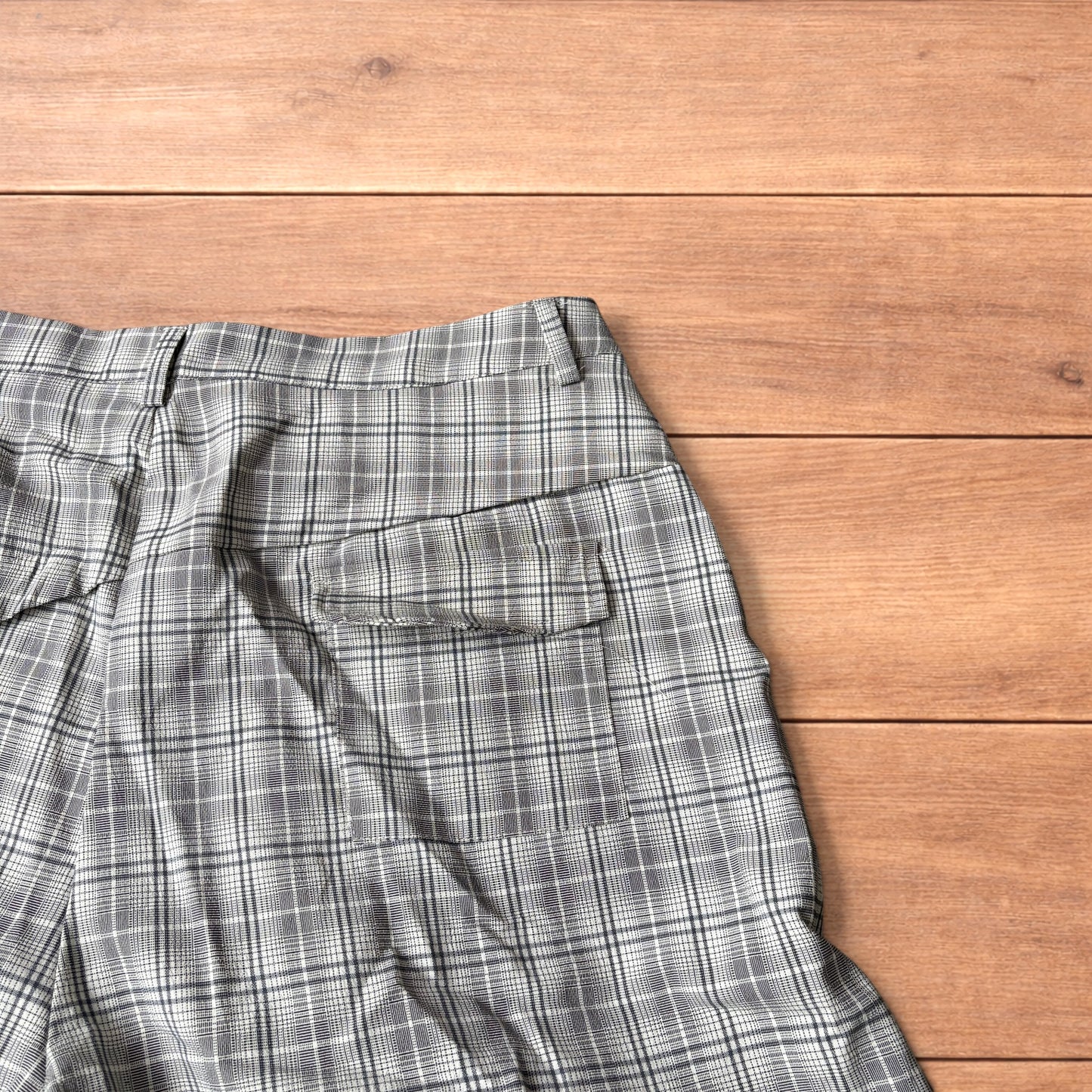 Baggy wide leg shorts with grey, beige and white checkered pattern laid flat on wooden floor showing front and back views