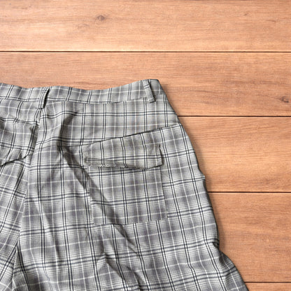 Baggy wide leg shorts with grey, beige and white checkered pattern laid flat on wooden floor showing front and back views