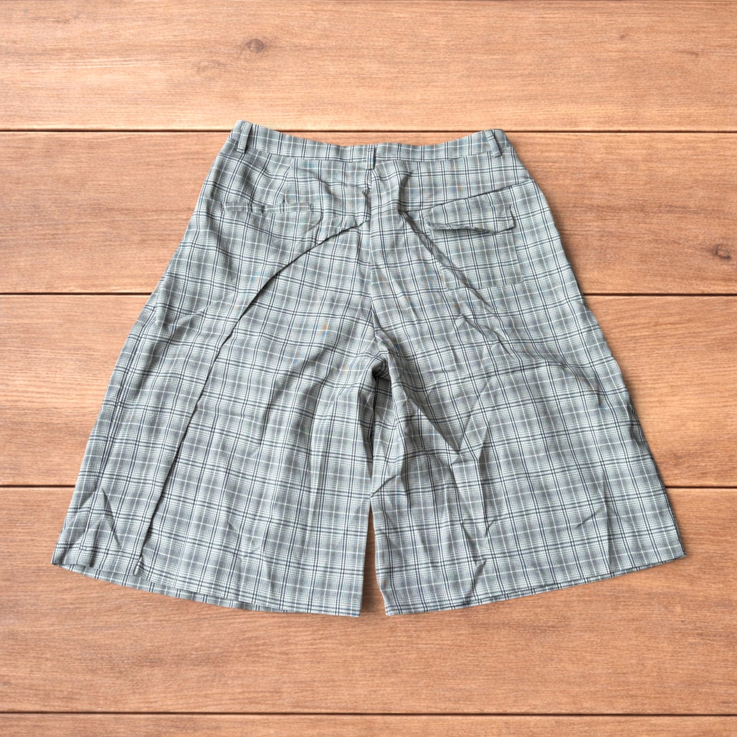 Baggy wide leg shorts with grey, beige and white checkered pattern laid flat on wooden floor showing front and back views