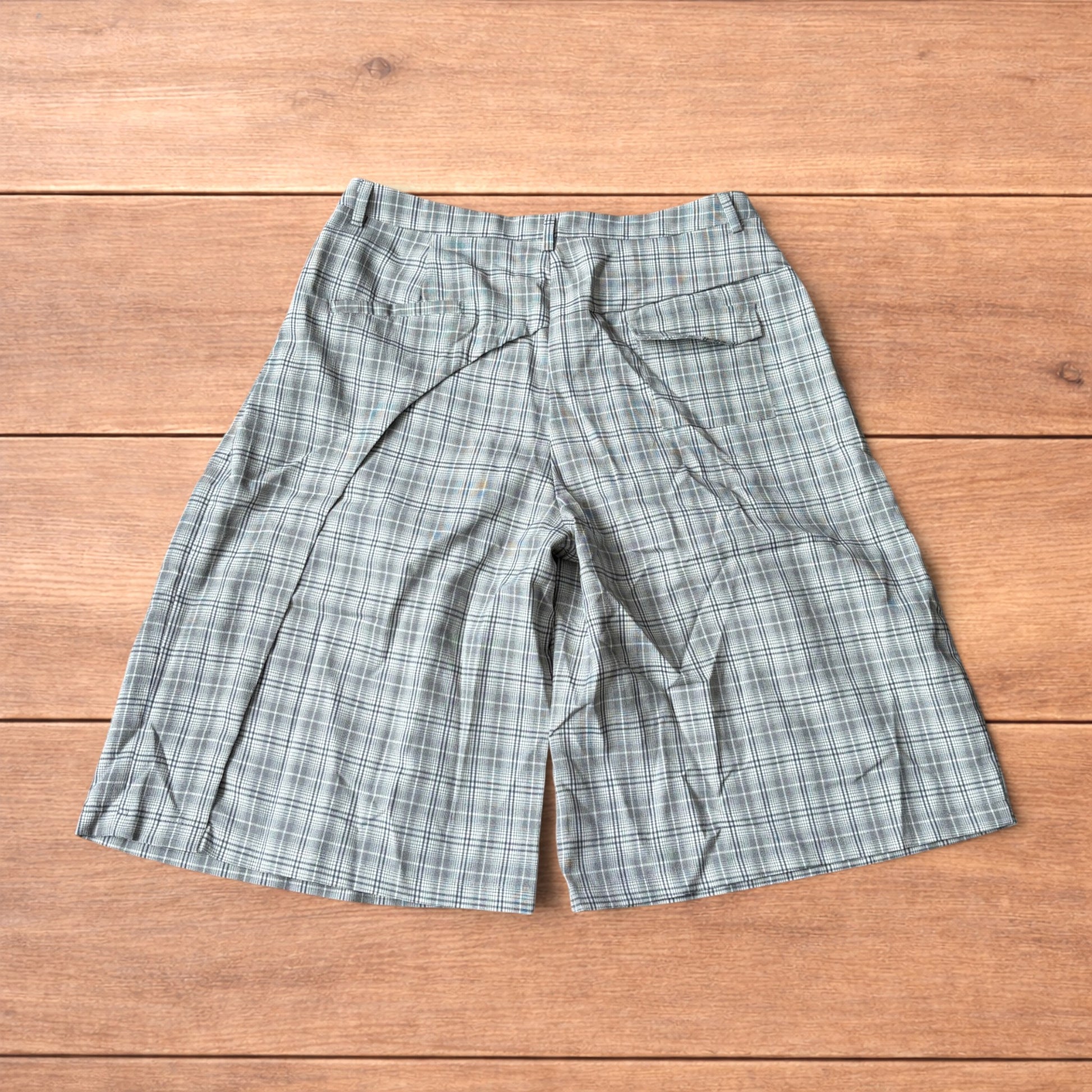 Baggy wide leg shorts with grey, beige and white checkered pattern laid flat on wooden floor showing front and back views